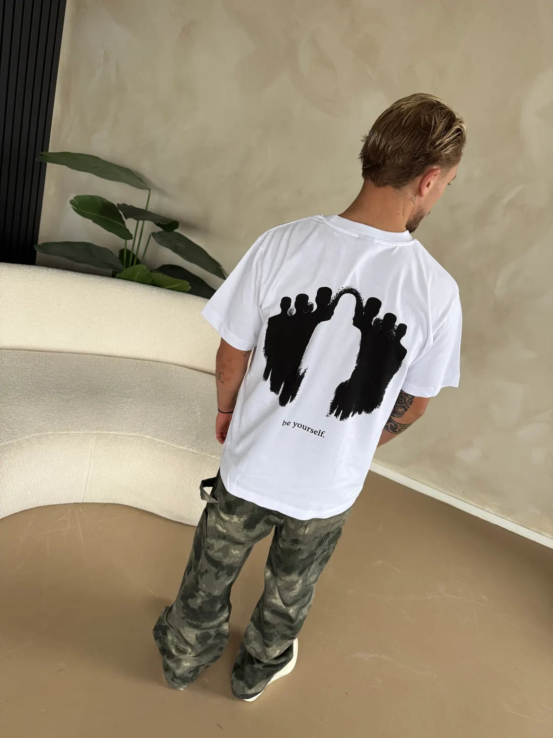 Een man in een wit shirt, van achteren gezien, met de print van Be Yourself op zijn rug.